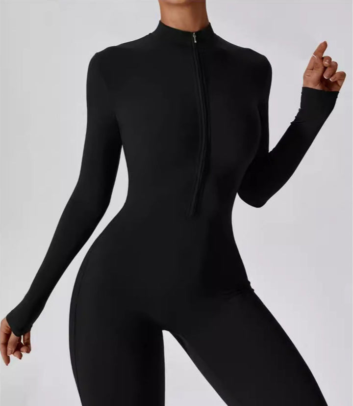 Femme portant une combinaison noire moulante à manches longues avec fermeture zippée frontale, assortie à des baskets blanches pour un look sportif et moderne.